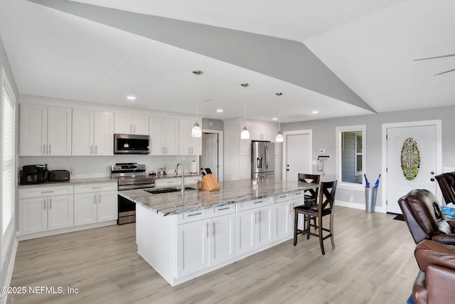 kitchen with appliances with stainless steel finishes, vaulted ceiling, light wood-type flooring, white cabinetry, and a sink