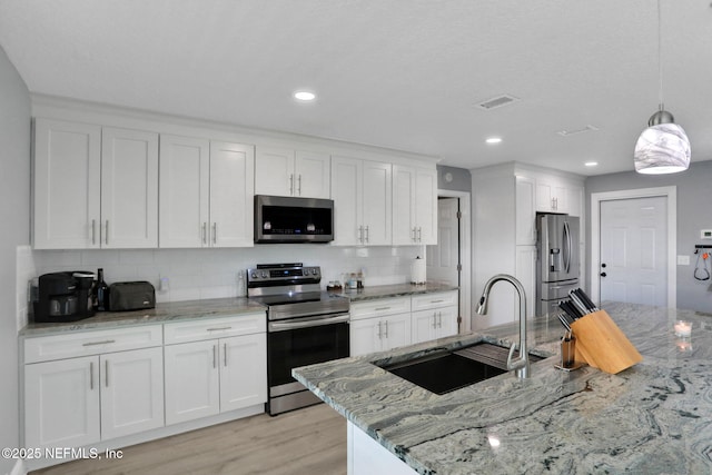 kitchen with visible vents, white cabinets, light stone counters, stainless steel appliances, and a sink