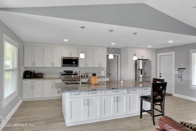 kitchen with stainless steel appliances, white cabinets, a sink, light stone countertops, and light wood-type flooring
