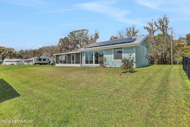 back of house with a lawn, a sunroom, roof mounted solar panels, fence, and metal roof