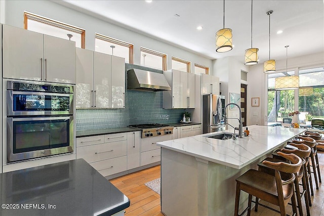 2446 Seminole Rd, Atlantic Beach, FL 32233 - kitchen featuring light wood-style flooring, a kitchen island with sink, stainless steel appliances, wall chimney range hood, and backsplash