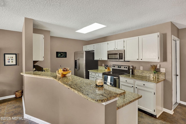 kitchen featuring appliances with stainless steel finishes, a peninsula, light stone countertops, a textured ceiling, and white cabinetry