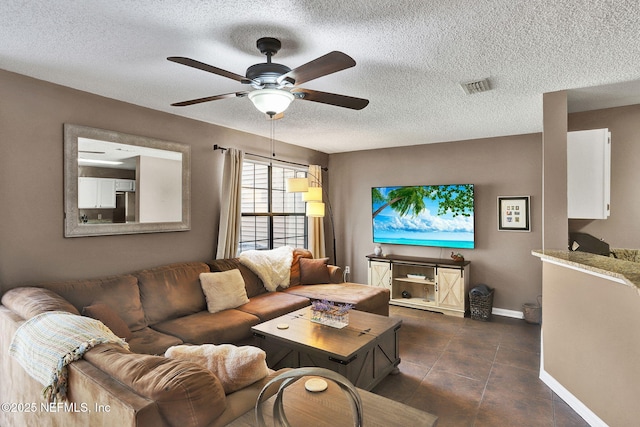 living area with ceiling fan, a textured ceiling, dark tile patterned floors, visible vents, and baseboards