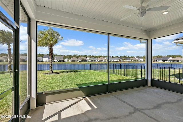 unfurnished sunroom with plenty of natural light, a ceiling fan, a residential view, and a water view