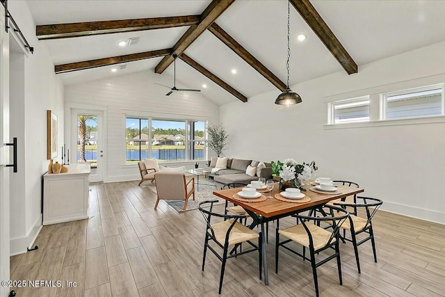 dining room with beam ceiling, a barn door, light wood-type flooring, and high vaulted ceiling