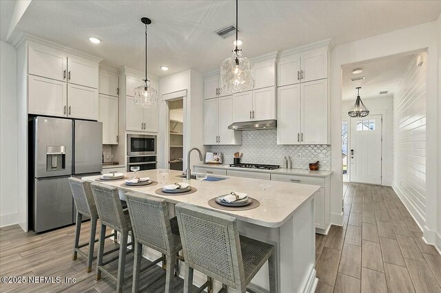 kitchen featuring a sink, under cabinet range hood, appliances with stainless steel finishes, white cabinetry, and tasteful backsplash