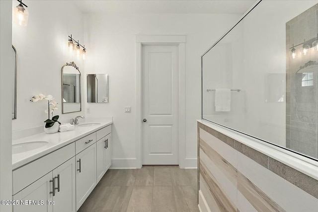 full bath with a tile shower, double vanity, baseboards, and a sink