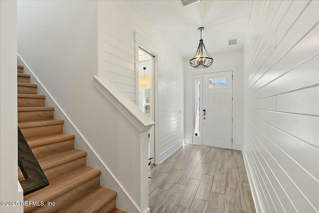 entrance foyer featuring stairway, visible vents, wood finish floors, wood walls, and a chandelier