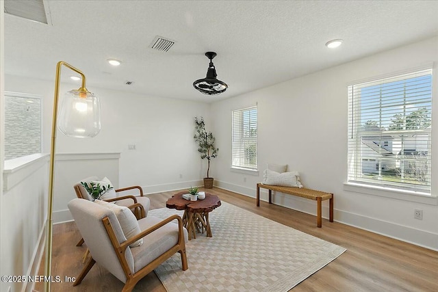 sitting room with a textured ceiling, light wood-style floors, visible vents, and baseboards