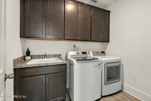 washroom with baseboards, light wood-type flooring, washer and dryer, cabinet space, and a sink