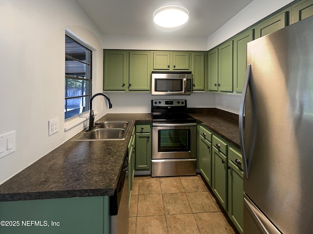 kitchen featuring stainless steel appliances, dark countertops, light tile patterned flooring, a sink, and green cabinetry