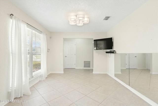 empty room with visible vents, a textured ceiling, and light tile patterned flooring