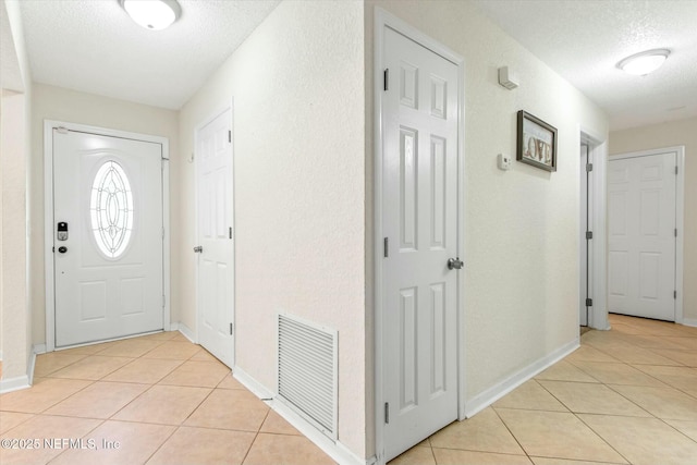 foyer with light tile patterned floors, baseboards, visible vents, and a textured ceiling