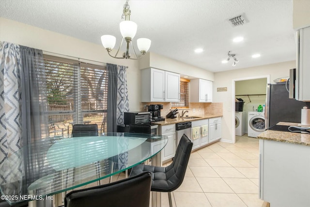 kitchen with light tile patterned floors, stainless steel appliances, visible vents, white cabinets, and washer and clothes dryer