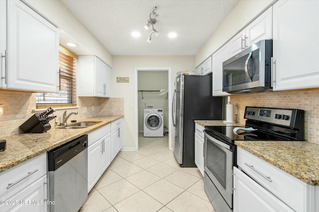 kitchen with stainless steel appliances, washer / clothes dryer, light tile patterned flooring, a sink, and white cabinets