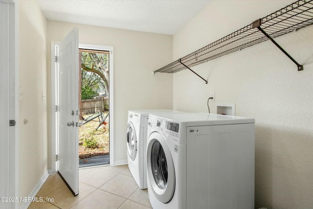 washroom with light tile patterned floors, a textured ceiling, washing machine and dryer, laundry area, and baseboards