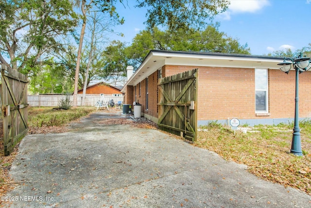 view of side of home with central AC unit, driveway, fence, and brick siding