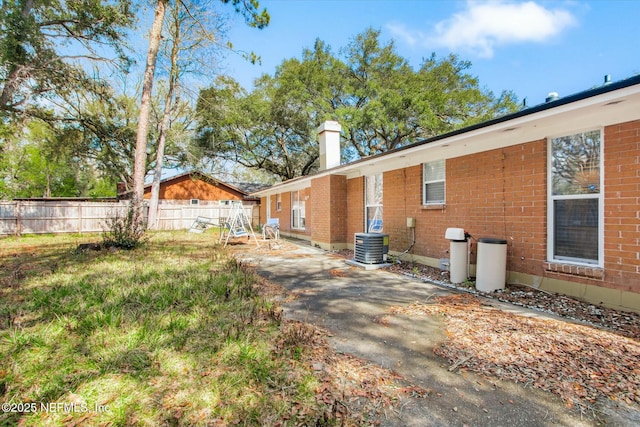 view of home's exterior featuring brick siding, a chimney, fence, and central air condition unit