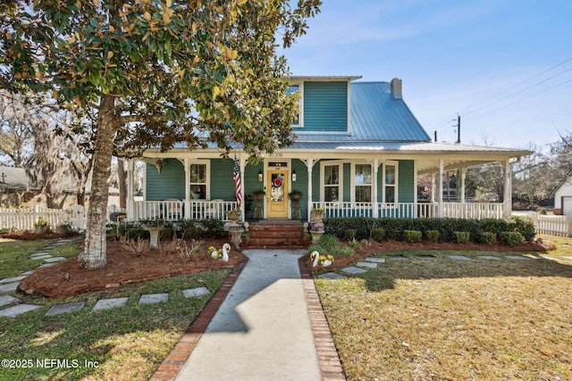 view of front of property with a chimney, covered porch, a front yard, metal roof, and fence