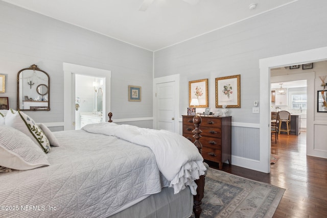 bedroom featuring ceiling fan, connected bathroom, dark wood-style flooring, and wainscoting