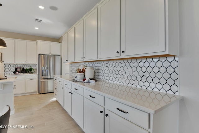 kitchen featuring visible vents, white cabinets, light countertops, stainless steel refrigerator with ice dispenser, and backsplash