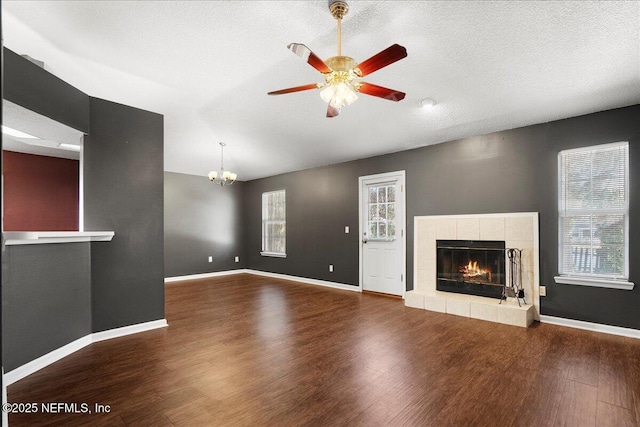 unfurnished living room with ceiling fan with notable chandelier, a tile fireplace, wood finished floors, and baseboards