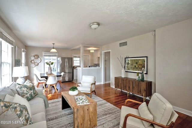 living room with visible vents, a textured ceiling, baseboards, and wood finished floors