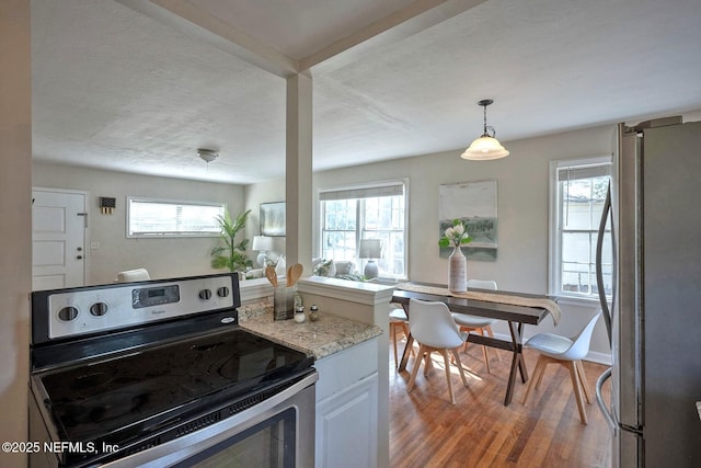 kitchen with light wood-type flooring, light stone counters, stainless steel appliances, baseboards, and hanging light fixtures