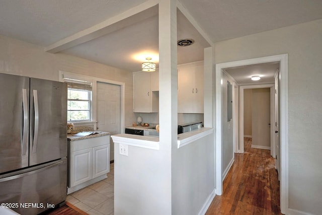 kitchen with visible vents, baseboards, light countertops, freestanding refrigerator, and white cabinets