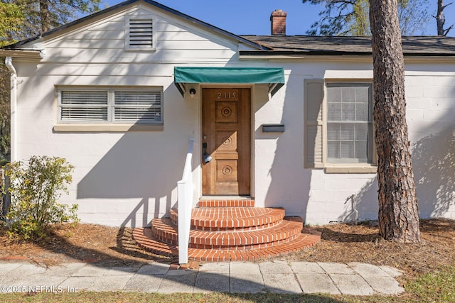 view of front of property featuring concrete block siding, a chimney, and a shingled roof