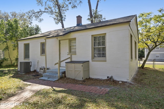 back of house with cooling unit, concrete block siding, a chimney, and fence