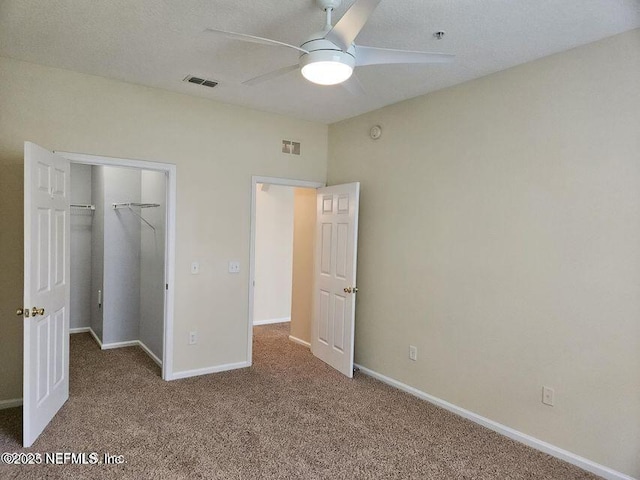 unfurnished bedroom with carpet floors, a walk in closet, visible vents, and baseboards