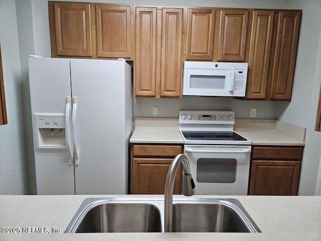 kitchen featuring light countertops, white appliances, a sink, and brown cabinets