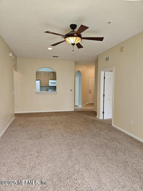 empty room with arched walkways, ceiling fan, carpet floors, visible vents, and baseboards