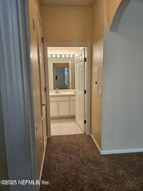 corridor with arched walkways, light tile patterned floors, light carpet, a sink, and baseboards