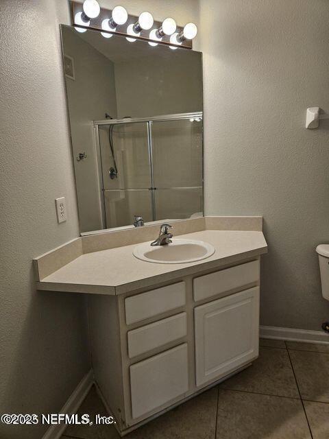 bathroom with baseboards, toilet, tile patterned floors, vanity, and a shower stall