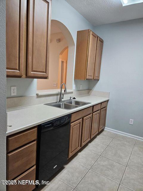 kitchen with black dishwasher, light countertops, a sink, and brown cabinets