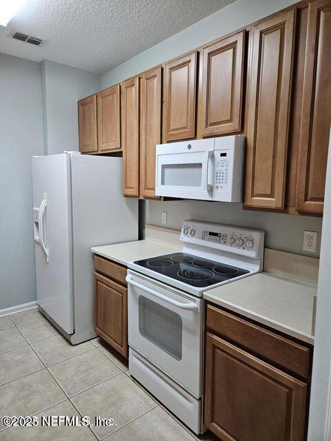 kitchen featuring light tile patterned floors, white appliances, visible vents, light countertops, and brown cabinetry