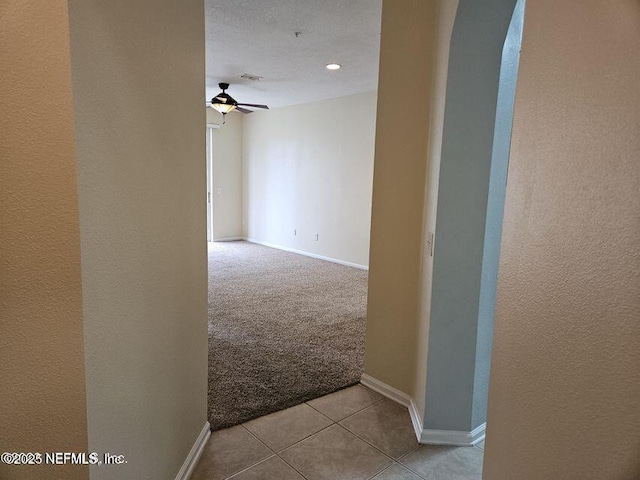 spare room featuring baseboards, light tile patterned flooring, a ceiling fan, and light colored carpet