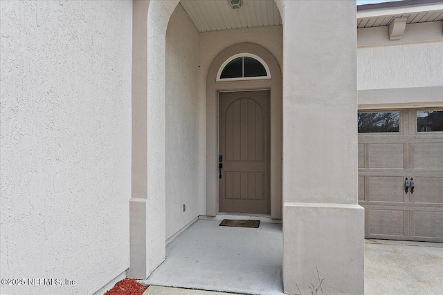 doorway to property with a garage and stucco siding