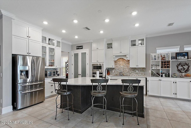 kitchen with stainless steel appliances, visible vents, a kitchen breakfast bar, a center island with sink, and glass insert cabinets