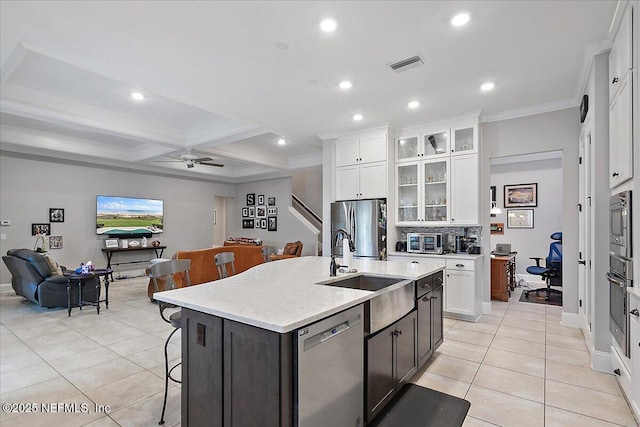 kitchen featuring a center island with sink, glass insert cabinets, appliances with stainless steel finishes, open floor plan, and white cabinetry