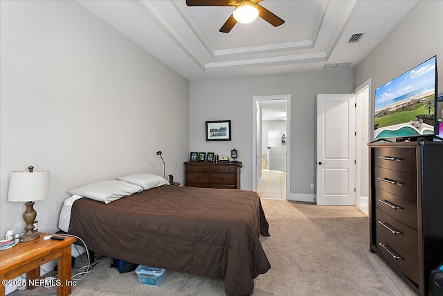 bedroom with a tray ceiling, light colored carpet, visible vents, ensuite bathroom, and ornamental molding