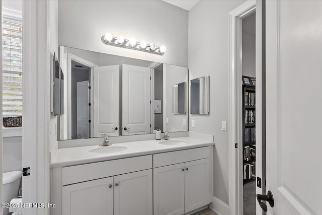 bathroom with a sink, toilet, and double vanity