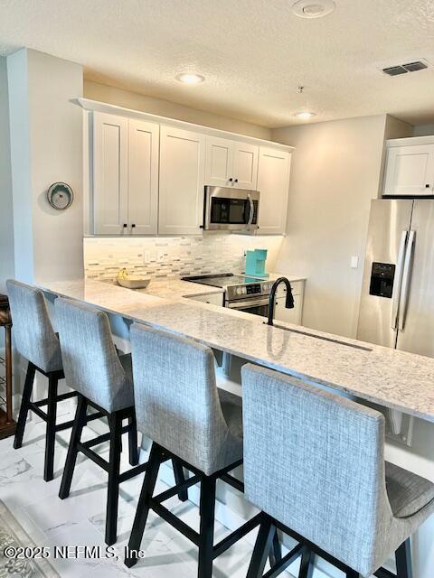 kitchen featuring visible vents, decorative backsplash, white cabinets, appliances with stainless steel finishes, and a sink