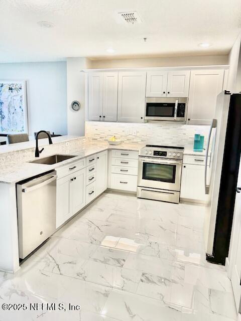 kitchen featuring a peninsula, a sink, white cabinets, marble finish floor, and appliances with stainless steel finishes