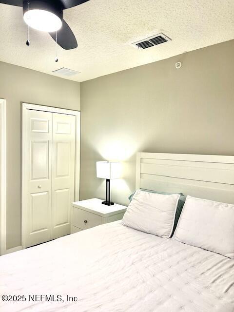 bedroom with a closet, visible vents, ceiling fan, and a textured ceiling