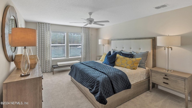 bedroom featuring light carpet, ceiling fan, visible vents, and a textured ceiling