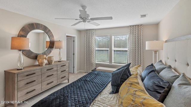 bedroom featuring light colored carpet, visible vents, ceiling fan, and a textured ceiling