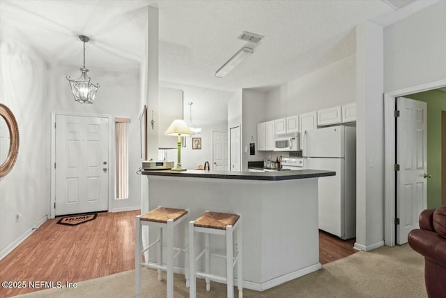 kitchen featuring white appliances, white cabinets, dark countertops, a breakfast bar, and decorative light fixtures